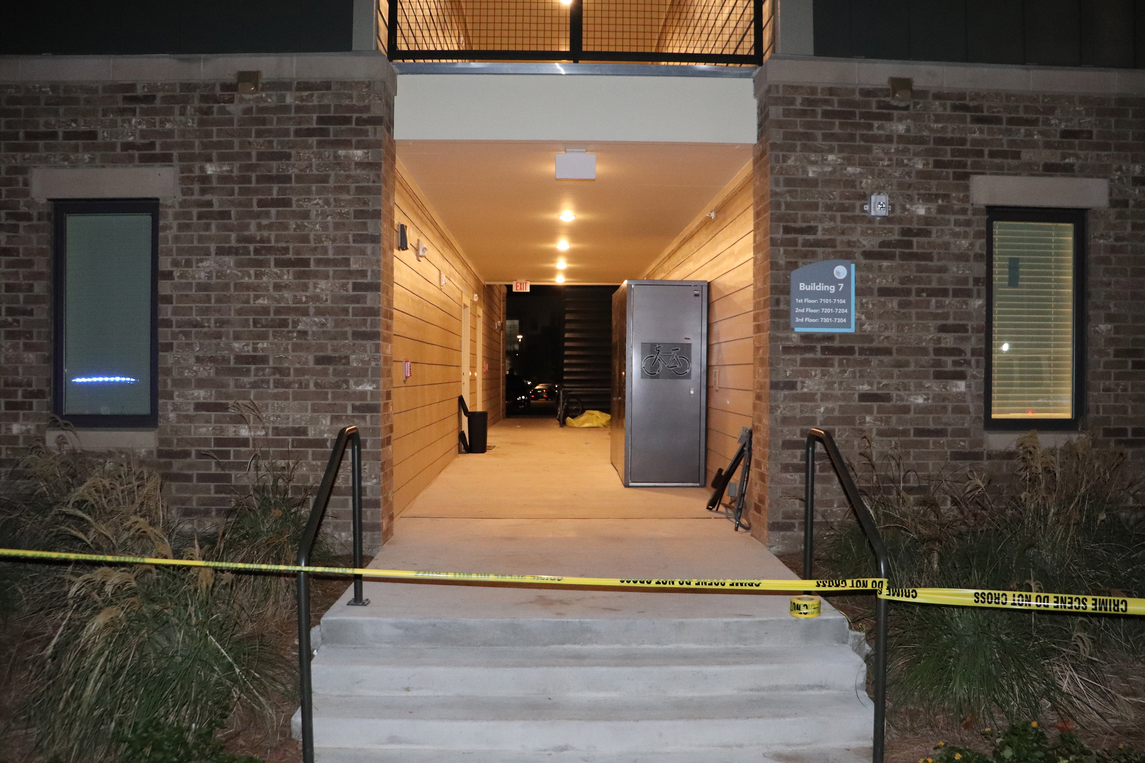 Yellow crime scene tape blocks the entrance to an apartment complex breezeway.