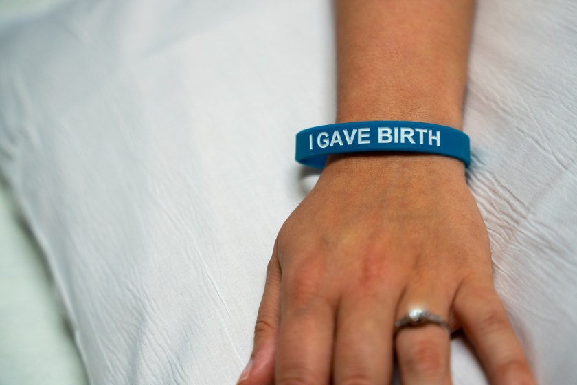 ecu_bracelet A photo of a woman's hand. She wears a blue wristband that reads, "I gave birth."