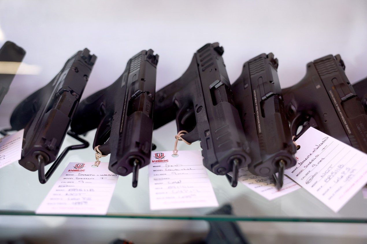 Five handguns rest on a glass shelf at a gun shop.