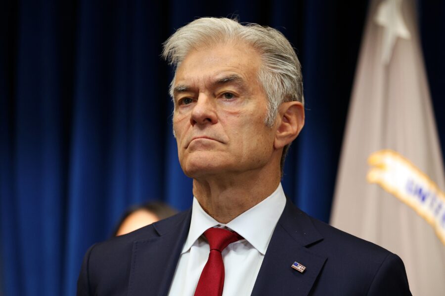 A senior man with grey hair wearing a navy suit and red tie