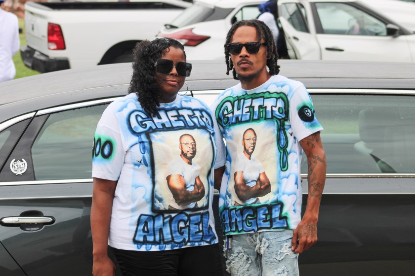 A man and a woman stand side-by-side wearing matching custom T-shirts with a photo of Lloyd Gilmore.