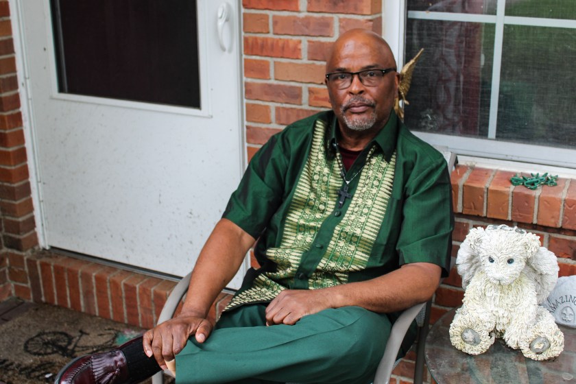 A man sits comfortably on a chair in front of his house.