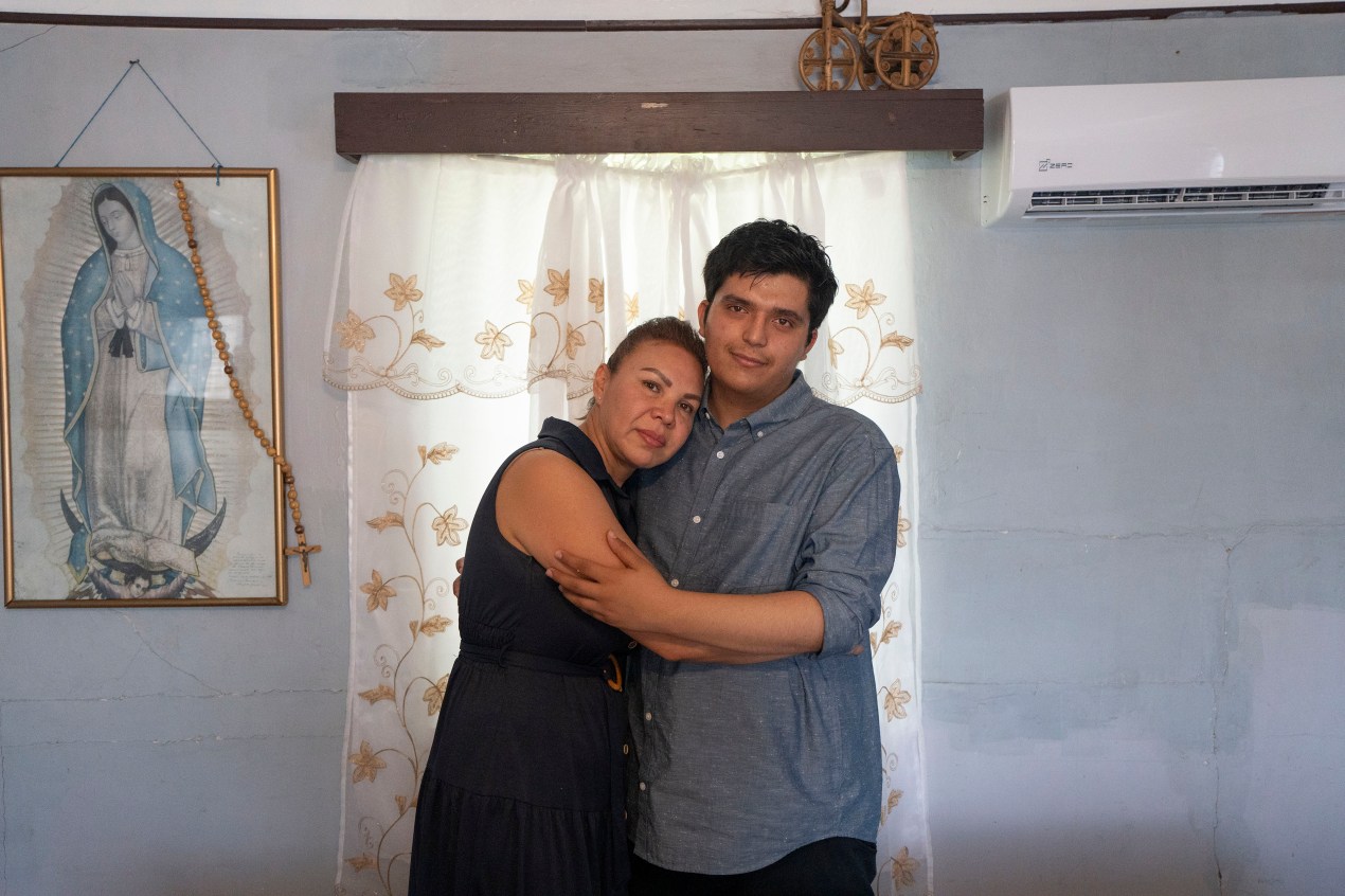 A man and woman embrace as they stand in front of a window and pose for a portrait