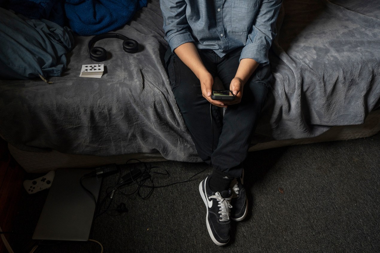 A person holds a smartphone as they sit on a bed