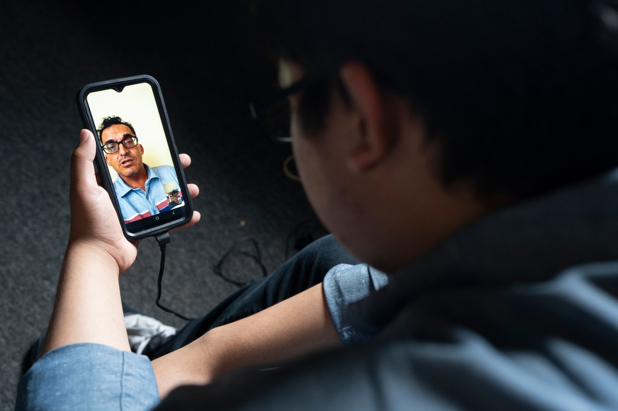 A man holds a smartphone with an image of a video chat with another man