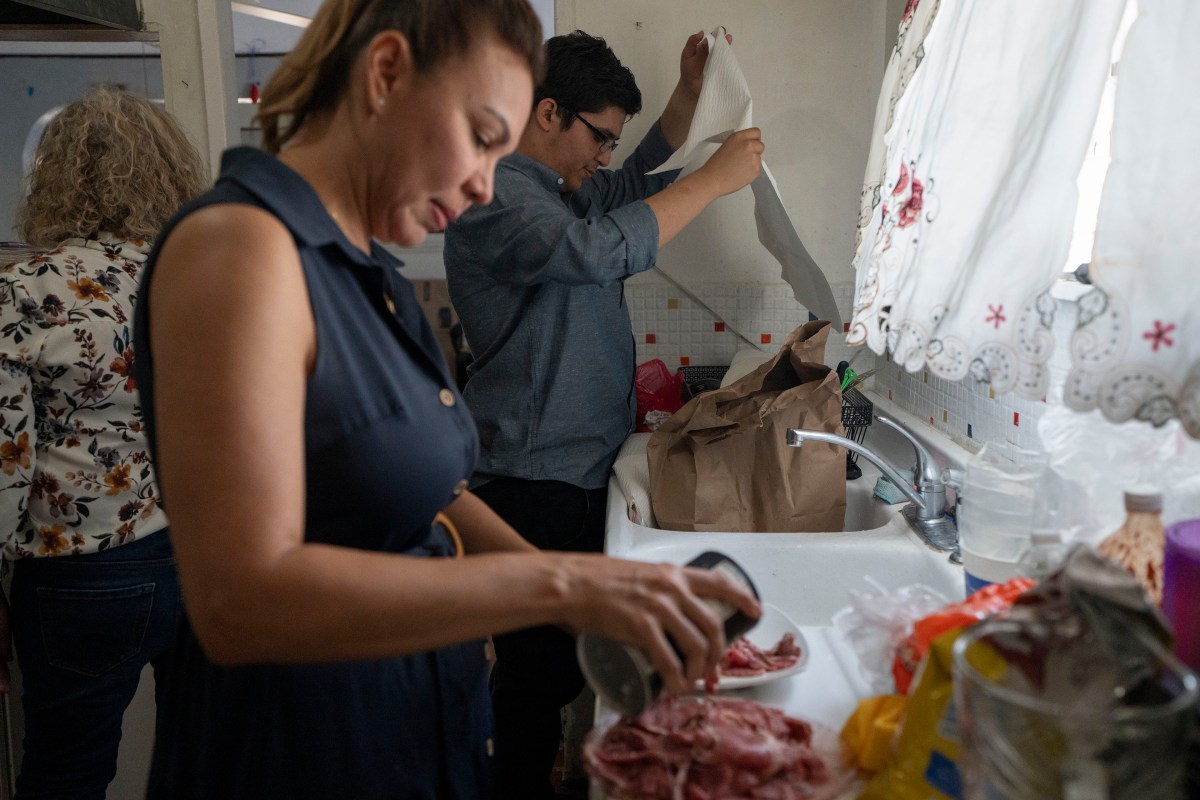 A man and woman stand in front of a sink and an open window as they prepare food in a kitchen