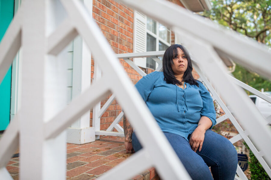 A woman sits on steps on her front porch.