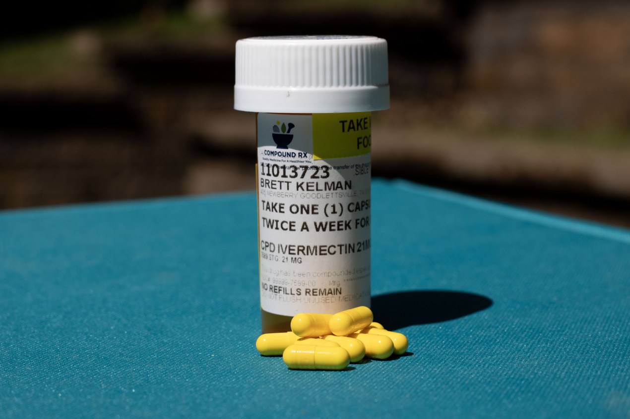 A photo of a pill bottle with a small pile of yellow pill capsules in front of it on a teal background.