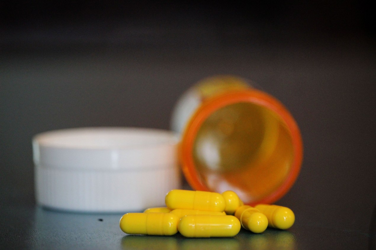 A close-up shot of ivermectin pill capsules. They are bright yellow, and an orange pill bottle is open, but blurred, in the background.