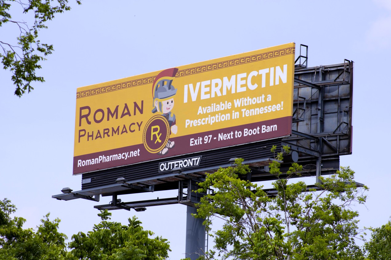 A billboard against a blue sky reads, "Roman Pharmacy / Ivermectin / Available Without a Prescription in Tennessee."
