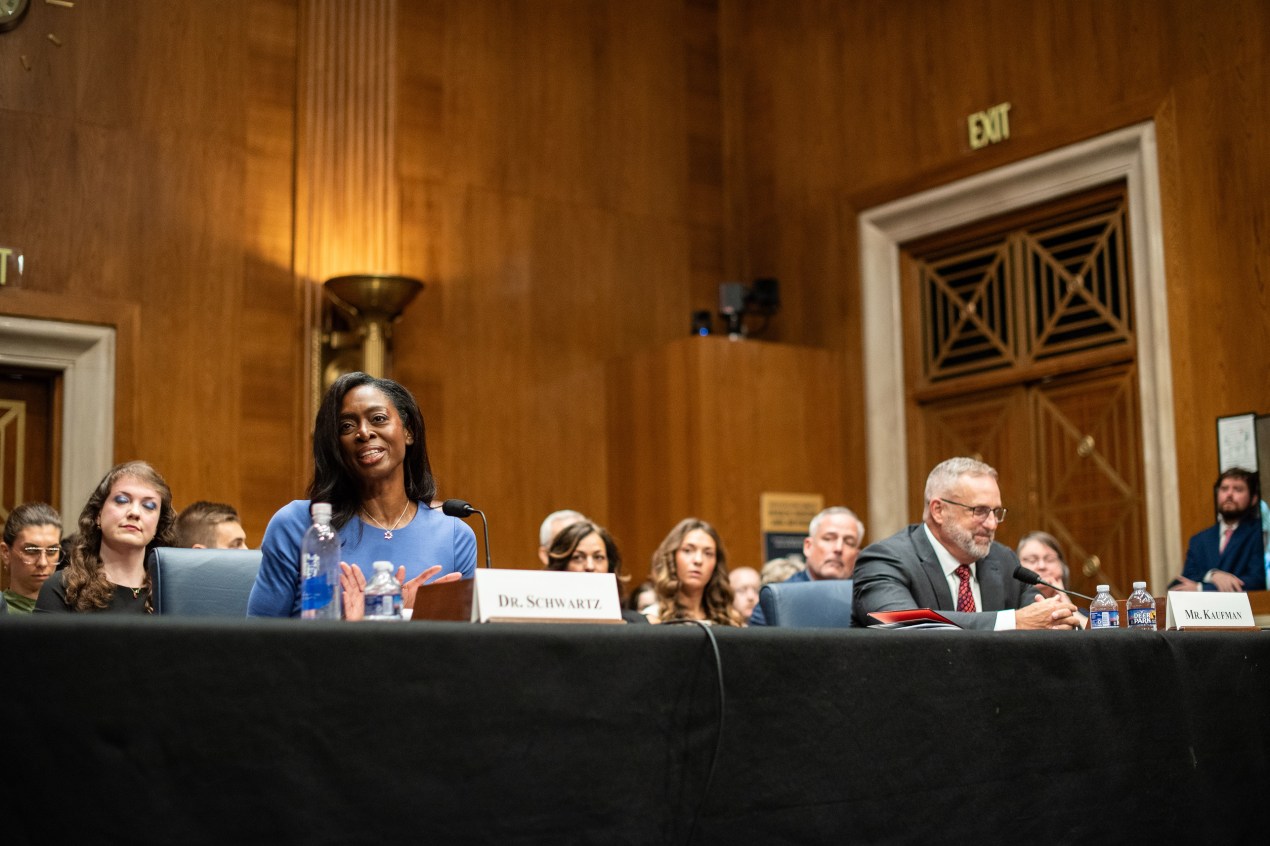 A wide shot of a Senate hearing room. Erica Schwartz and Sean Kaufman sit next to each other at the witness table.