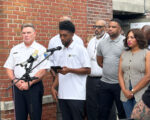 Mayor Brandon Scott speaks at a microphone outside. City officials stand behind him.