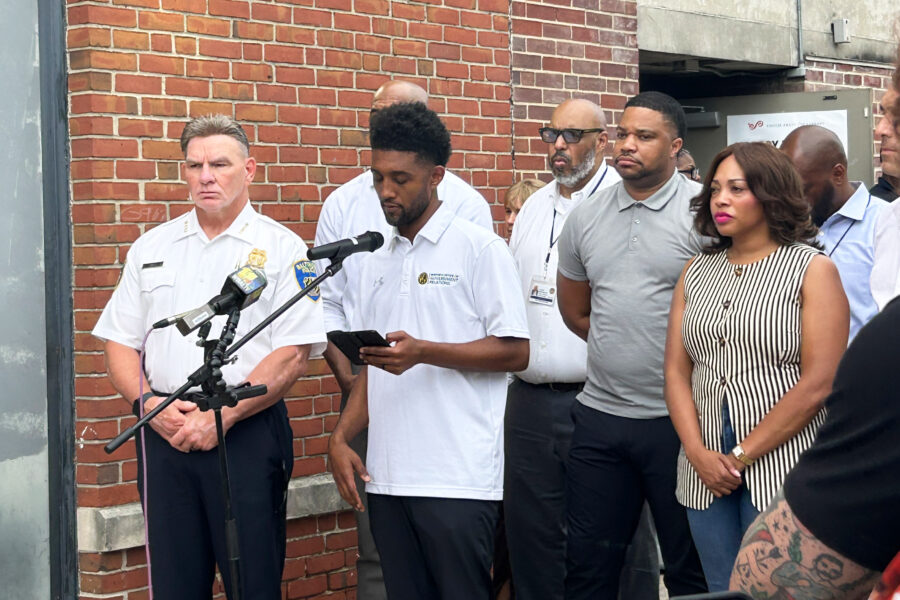 Mayor Brandon Scott speaks at a microphone outside. City officials stand behind him.