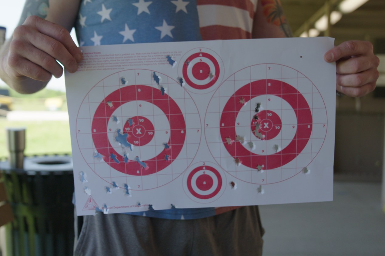 targets A pair of hands holds up a piece of paper with two large bull's eye targets and two small ones. Bullet holes are scattered across the paper.