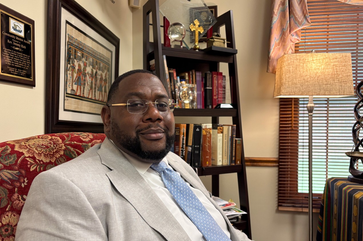 thomasville_07-min A Black man sits in an interior room. A placard, art print, and bookshelf are seen behind him.