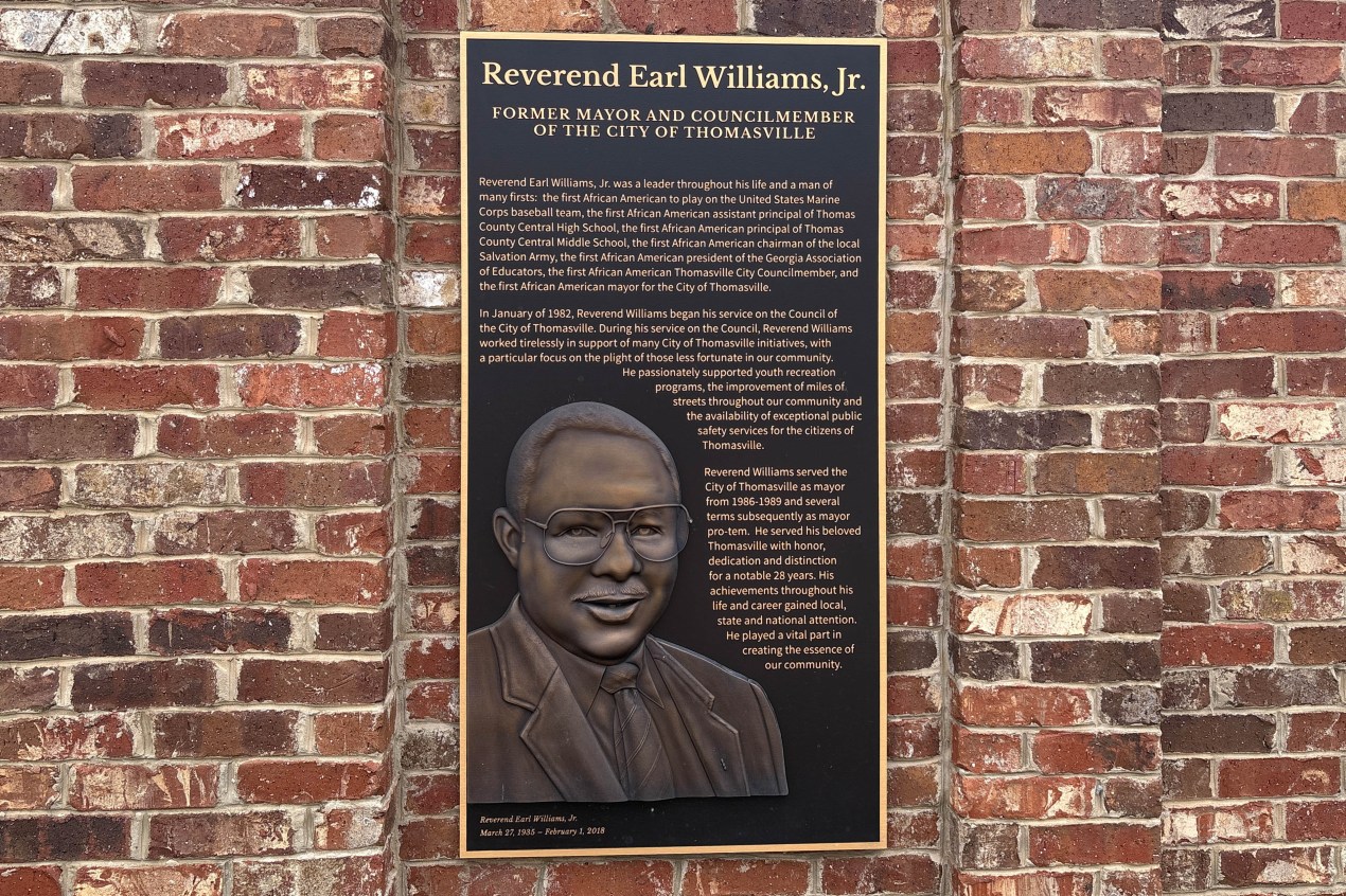 thomasville_08-min A plaque on a brick wall with the name and biography of Rev. Earl Williams Jr. The plaque also has a bas-relief sculpture of Williams.