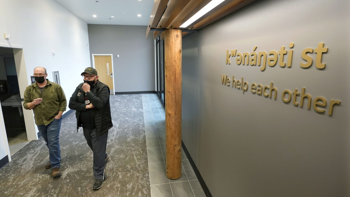 Two men walk beside each other in the hallway of a health clinic. Signage on the wall reads, "we help each other."