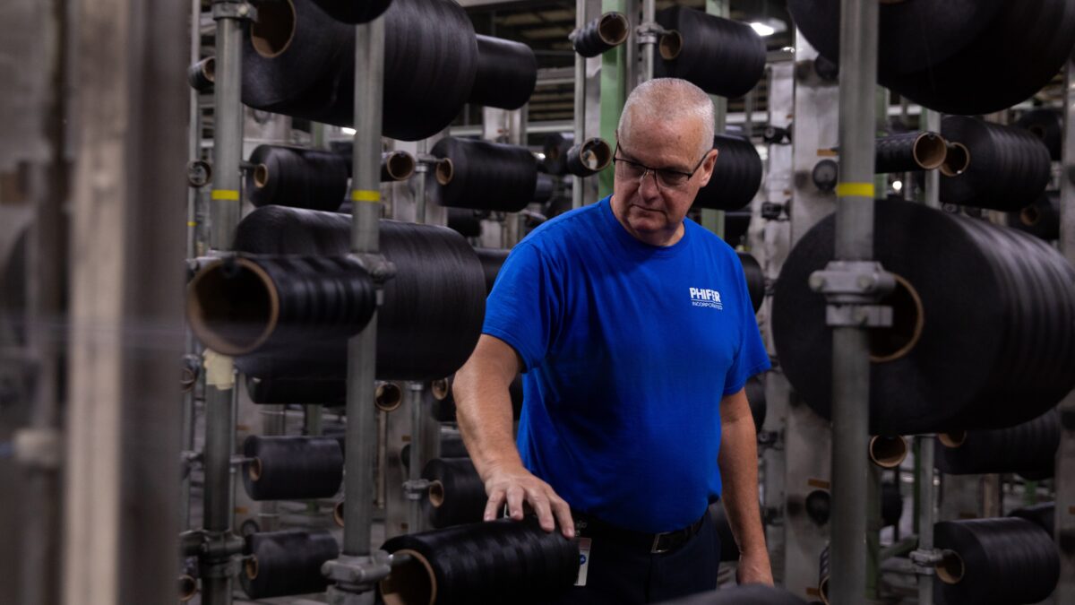 A man in a blue tshirt and glasses stands in a factory