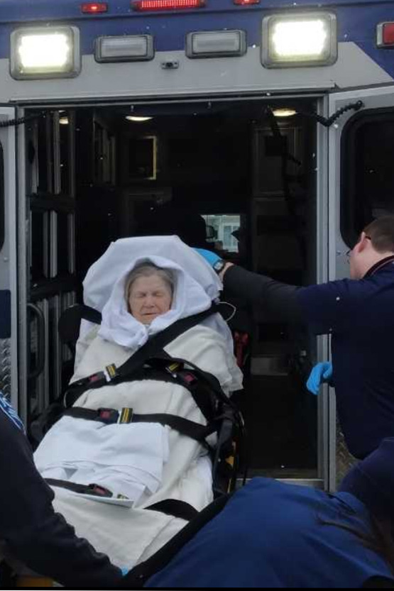 A senior woman in a stretcher is loaded into an ambulance.