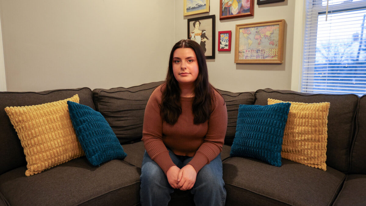 A 25-year-old woman sits on a couch and looks directly towards the camera.