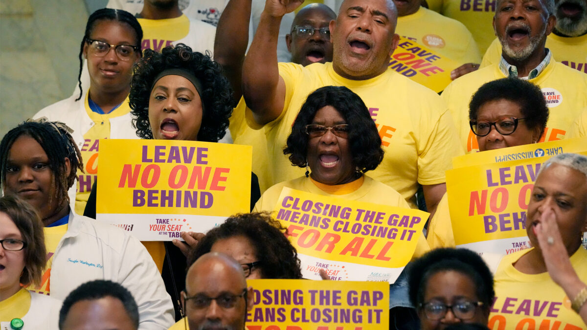 A photo of a group of activists holding signs that read, "Leave no one behind," and "Closing the coverage gap means closing it for all."