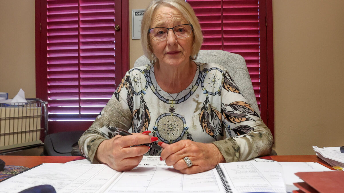 A photo of a woman seated at her desk. Paperwork is in front of her and she is holding a pen in her hands.