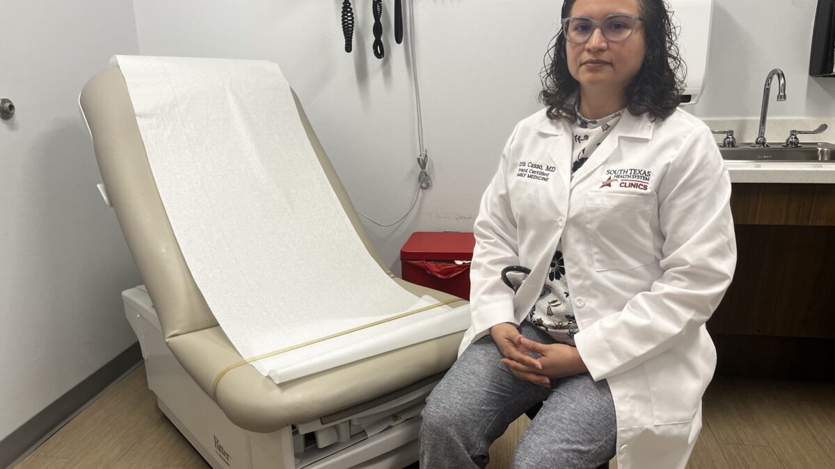 A photo of a doctor sitting by an exam chair in her office.