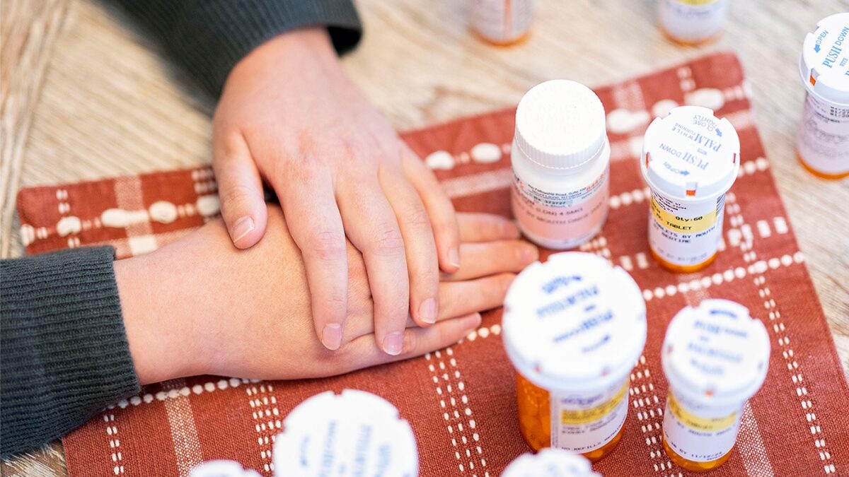 Sheldon Ekirch with her hands folded on a table next to her pill bottles.