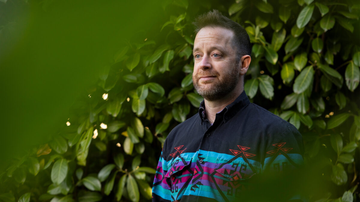 A photo of a man standing outside for a portrait by some shrubbery.