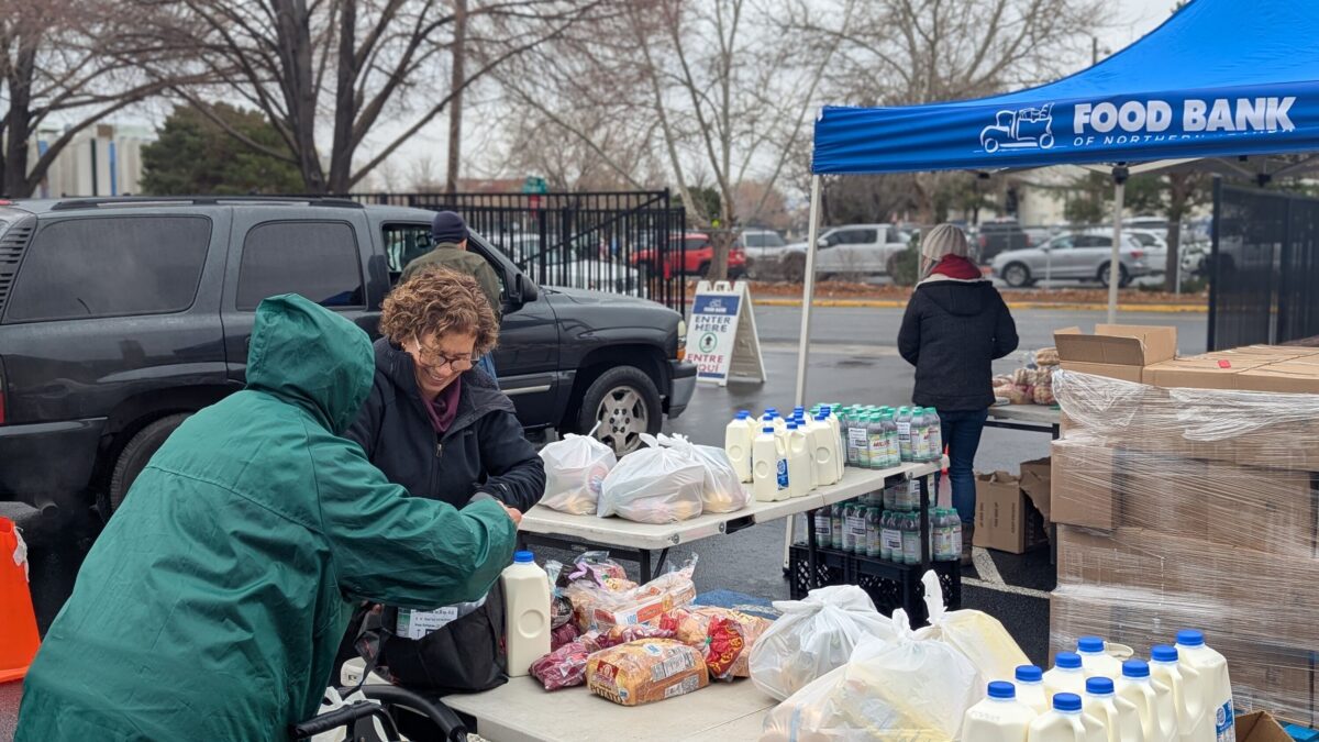 A photo of food bank attendees picking up loaves of bread, half-gallons of milk, and bags of produce.