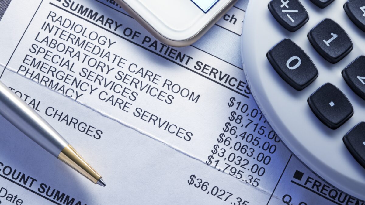 A calculator, smart phone, and a ballpoint pen rest on top of a very expensive medical bill.