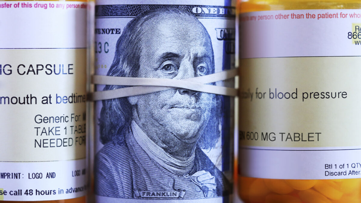 A roll of one hundred dollar bills sits among a row of prescription medication bottles.