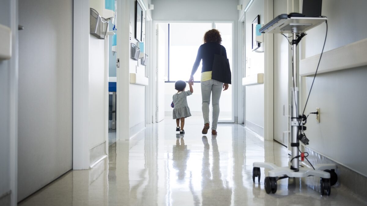 A woman and child walk hand in hand down a hospital corridor