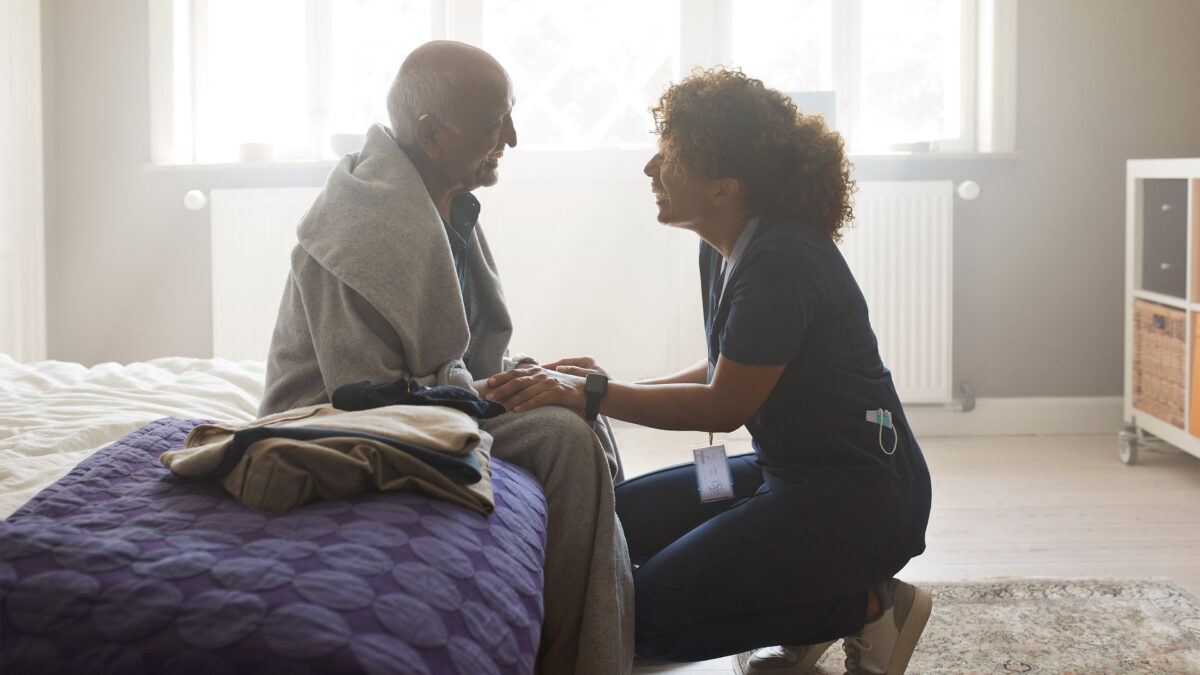 A nurse offers home care to an elderly male patient.