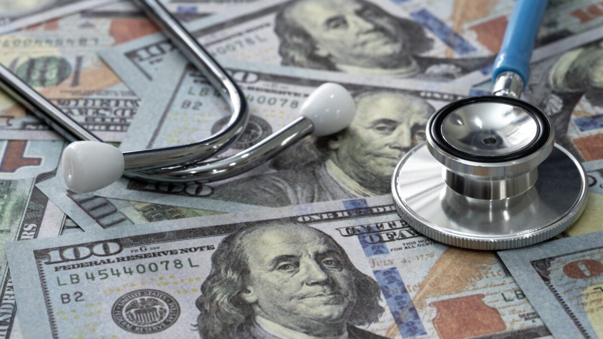 A stethoscope atop hundred-dollar bills on a flat surface.