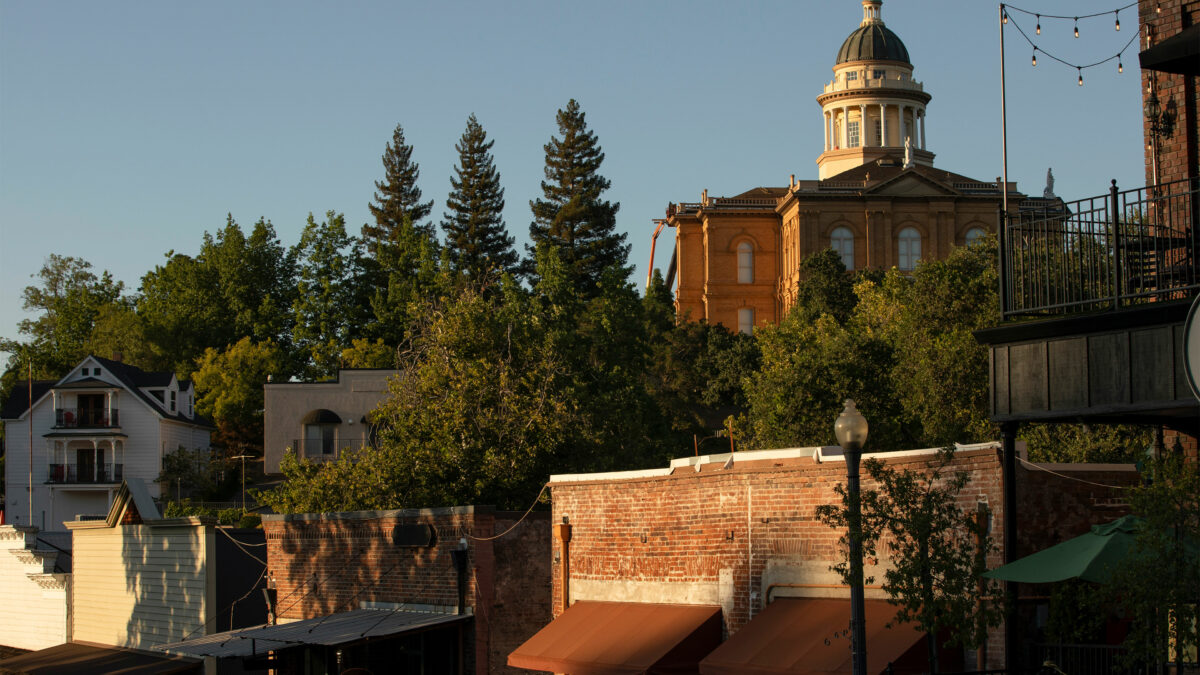 A photo of a historic downtown area of Auburn, California. Old buildings are seen alongside trees. A rotunda is seen on top of a tall building in the background.
