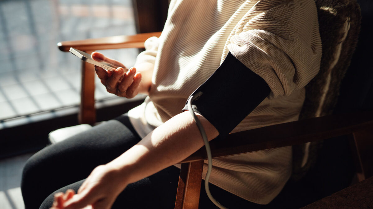 A photo of a woman sitting in a chair from the shoulders down. She is taking her blood pressure.