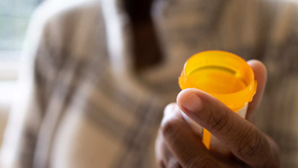 A photo of a hand holding an opened pill bottle.