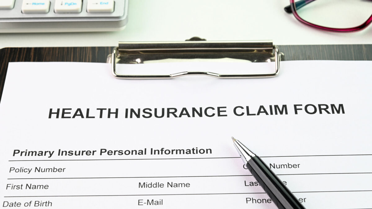 A health insurance claim form on a clipboard. A black pen rests on top.