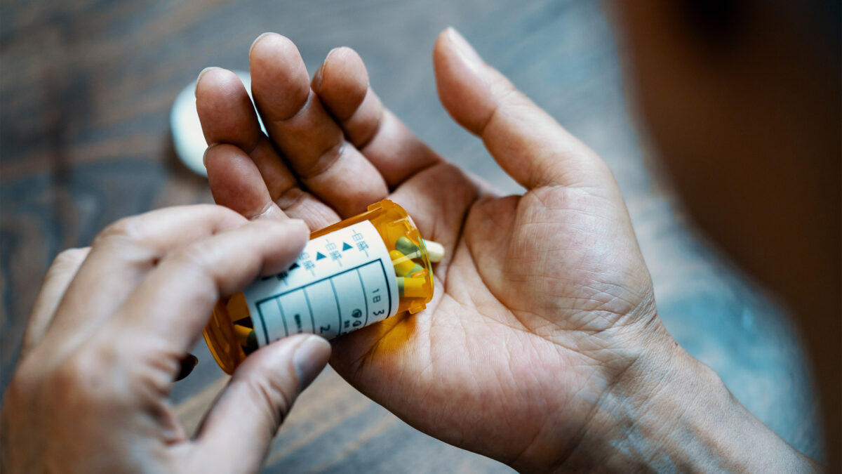 A photo of a man pouring pills into his hand.