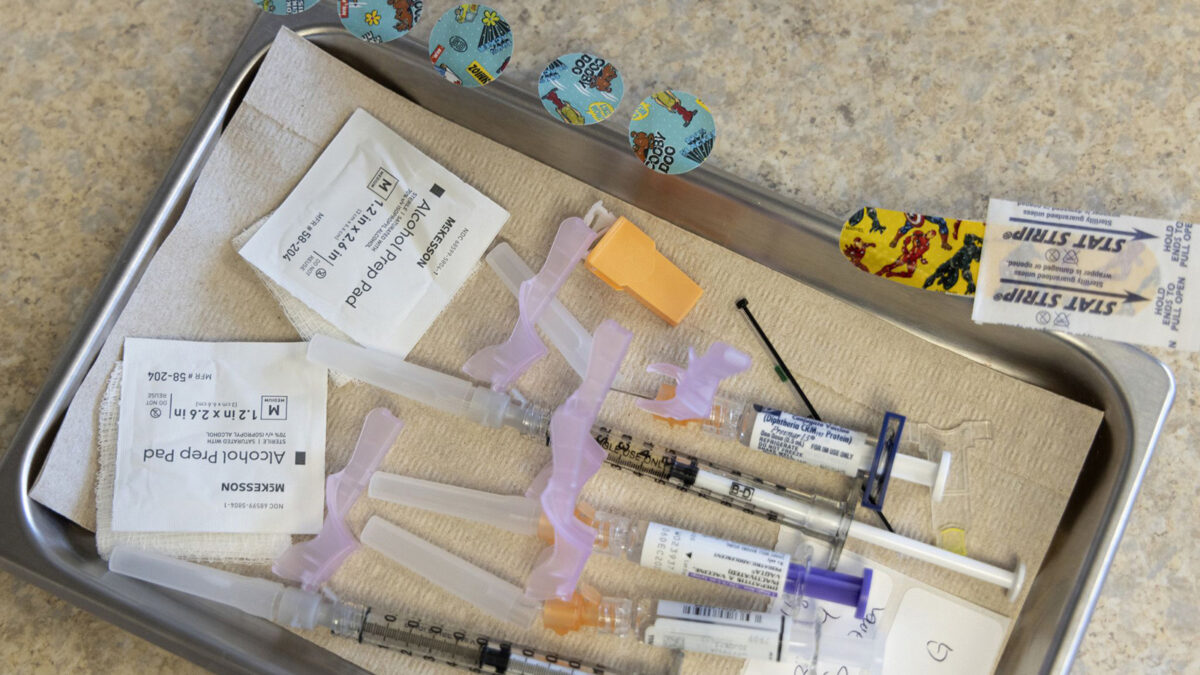 Alcohol pads, syringes, vaccines, and bandages lie on a tray at a pediatrician's office