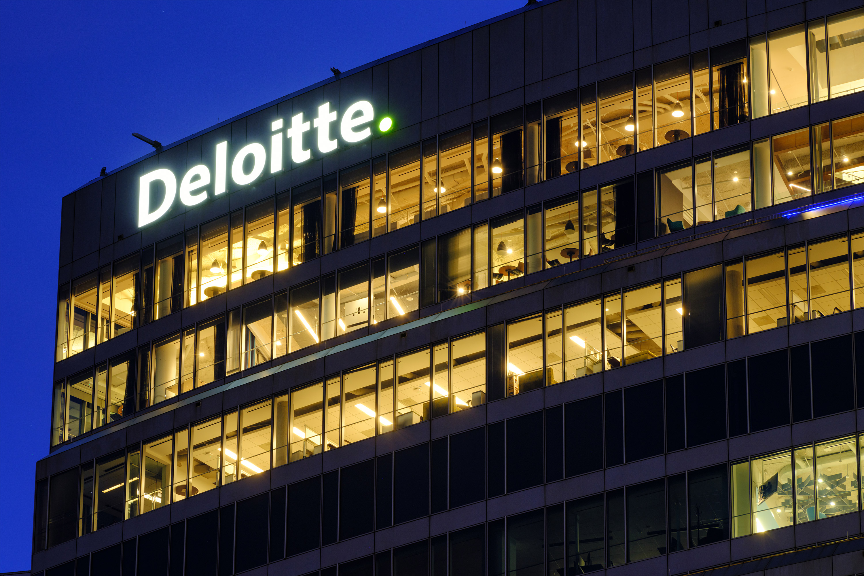 gettyimages-2034032777-resized A photo of a Deloitte office building taken at dusk, with the company's logo on the building lit.