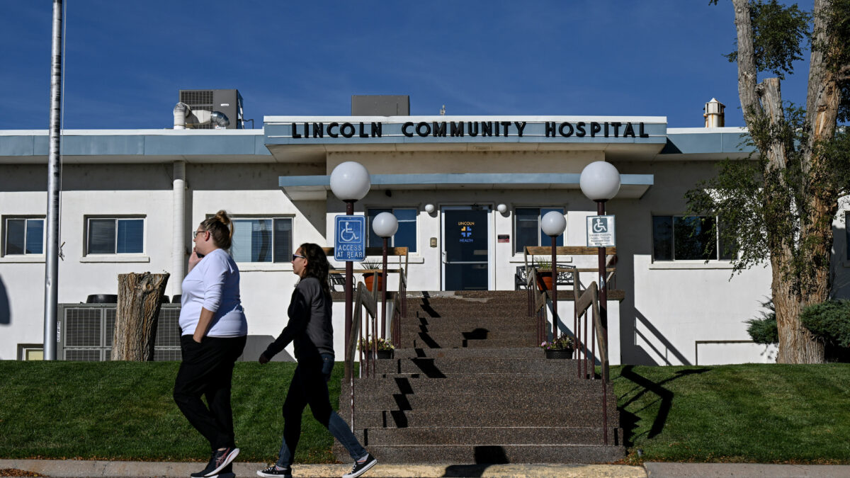 A photo of the exterior of a community hospital in rural Colorado. Two pedestrians walk across the sidewalk in front of it.
