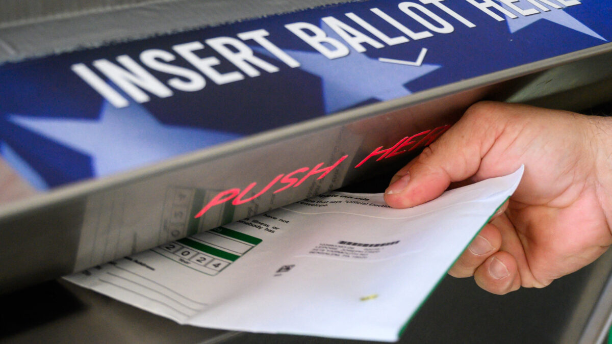 A photo of a person putting their ballot into a drop off box.