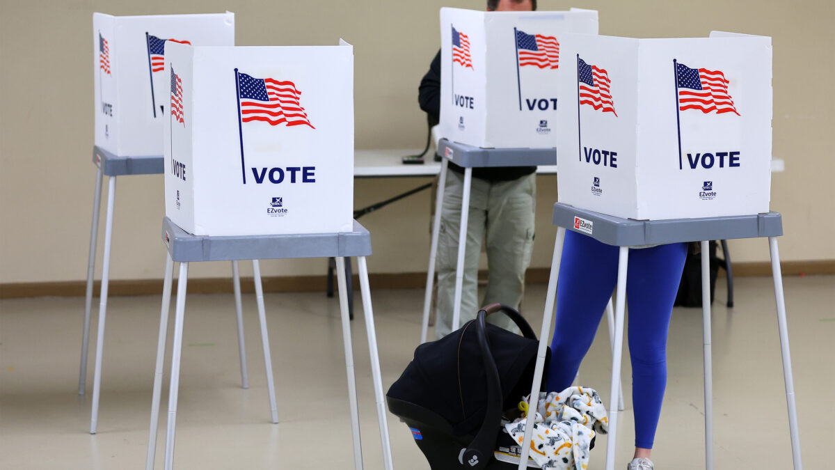 A photo of two voters — a man in the back and a woman with a baby carrier in the front.