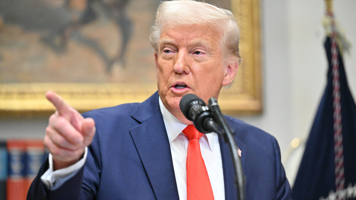 A photo of President Trump at the White House speaking into a microphone, pointing with his hand.