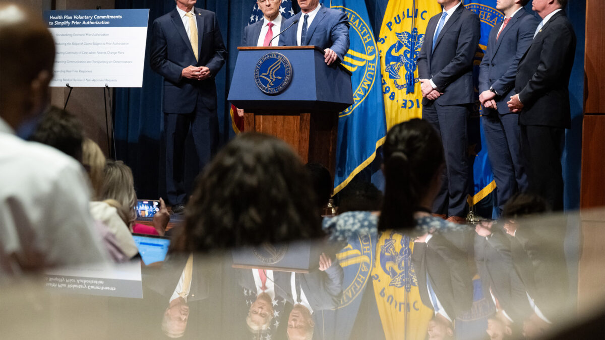 A photo of Robert F. Kennedy speaking at an official HHS news conference surrounded by others on a stage.