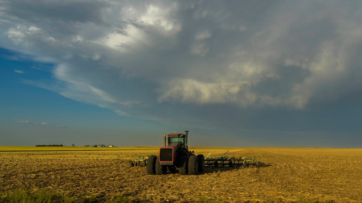 A tractor is parked in a field. Dark clouds are moving overhead.