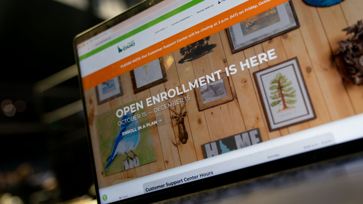 A laptop screen shows Idaho's Affordable Care Act marketplace website, with "Open Enrollment Ends December 15" in all-cap tyoe.