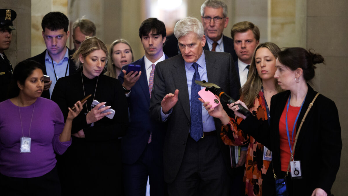 A photo of Sen. Cassidy walking as reporters flank him on both sides.